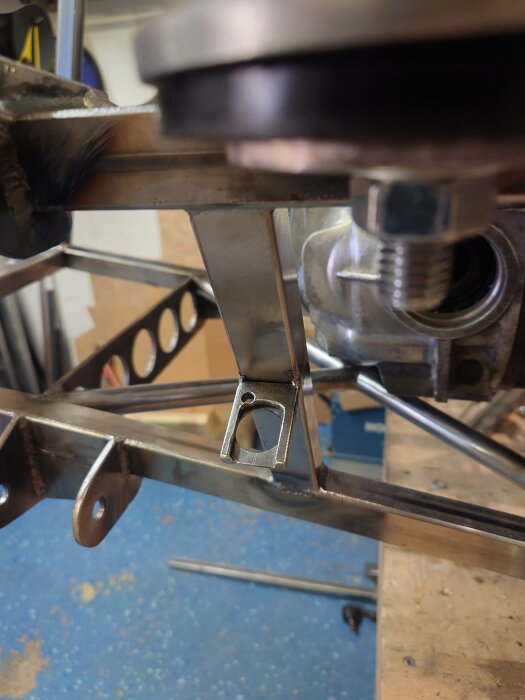 Metallfäste på ett fordonchassi med närliggande strukturer och komponenter i en verkstadsmiljö.