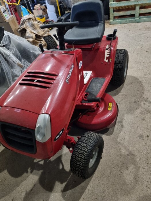 Röd Murray trädgårdstraktor parkerad i ett garage, använd för transport och gräsklippning.