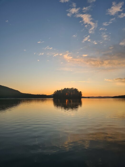 Solnedgång vid en sjö med en ö silhuetterad mot en spegelblank vattenyta och färggrann himmel.