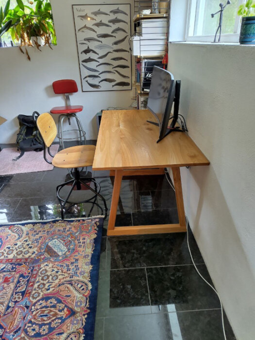 Hemsnickrat skrivbord av almträ med en datorskärm, placerat i ett ljust rum.