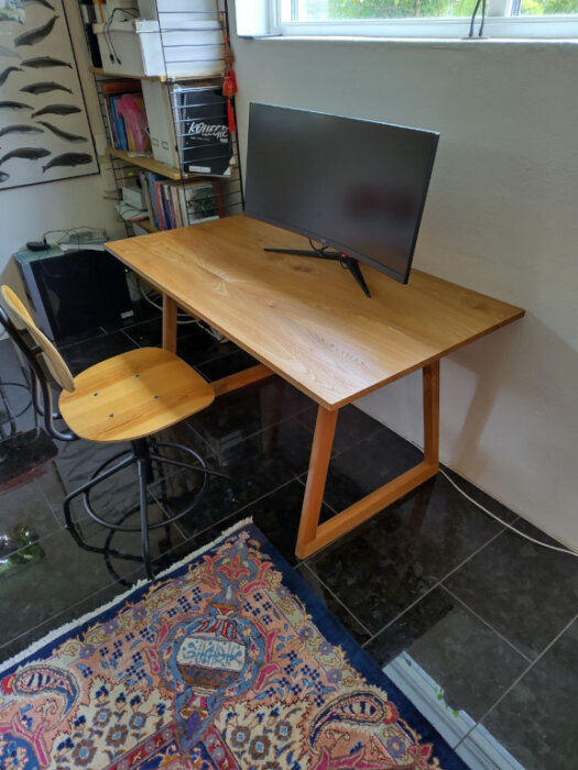 Hemsnickrat skrivbord i alm med platt TV-skärm ovanpå, bredvid en trästol och på ett orientaliskt matt.