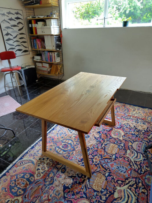 Handgjort skrivbord i almträ, placerat i ett rum med bokhylla och mönstrad matta.