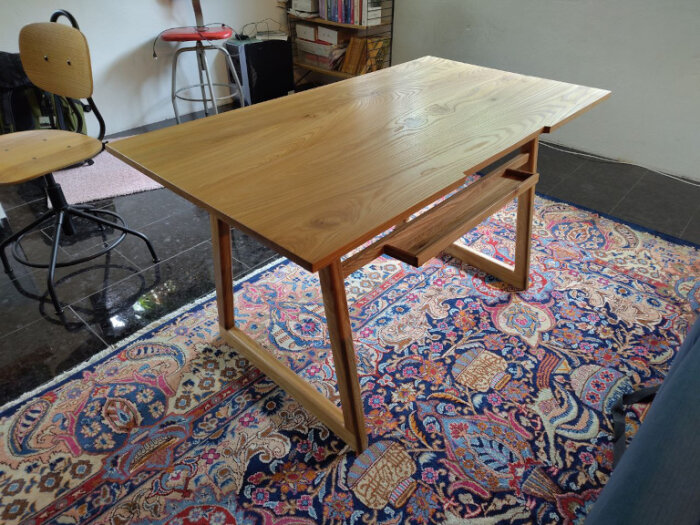 Hantverksmässigt tillverkat skrivbord i almträ på en orientalisk matta, med arbetsstol i bakgrunden.