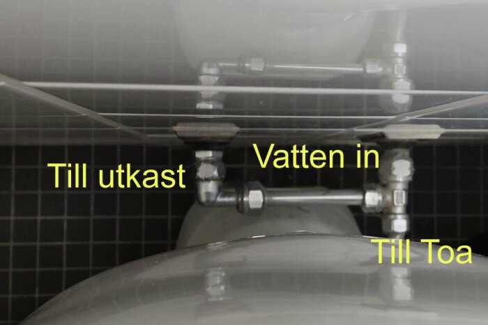 Installation av vattenledningar märkta med 'Vatten in', 'Till Toa' och 'Till utkast' bakom toalett.