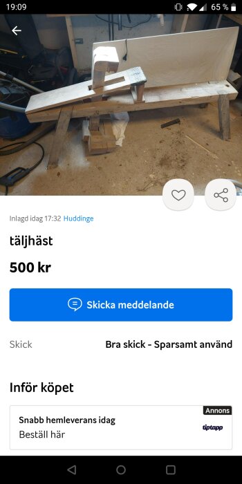 Trähäst (täljhäst) i verkstadmiljö med verktyg och byggmaterial i bakgrunden.