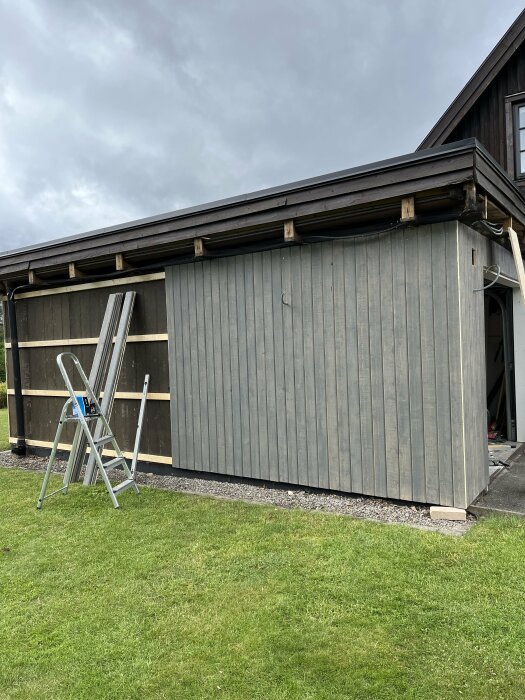 Grå z-panel stående på garageväggen med synliga glespaneler ovanpå, en stege lutad intill, under arbete.