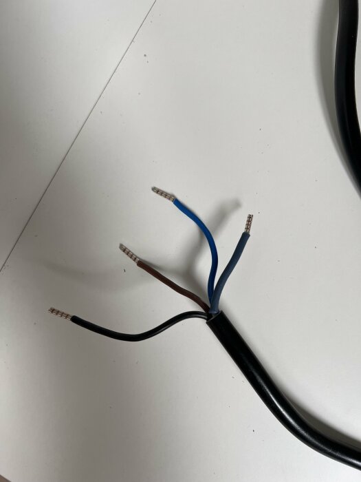 Skalad elektrisk kabel med synliga koppartrådar i blått, brunt och svart på vit bakgrund.