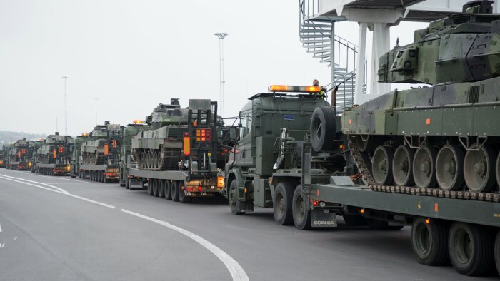 Konvoj av militära lastbilar som transporterar stridsvagnar på en väg.