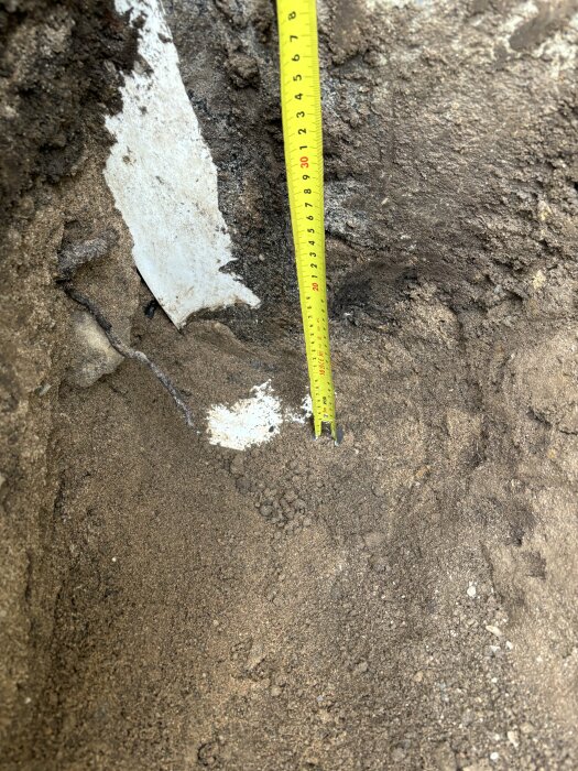 Måttband mot markyta för att mäta djupet på en möjlig grund eller grävning.