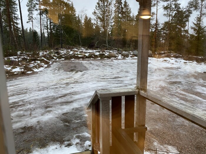 Utsikt från ett hus på landsbygden med smältande snö och skog i bakgrunden.