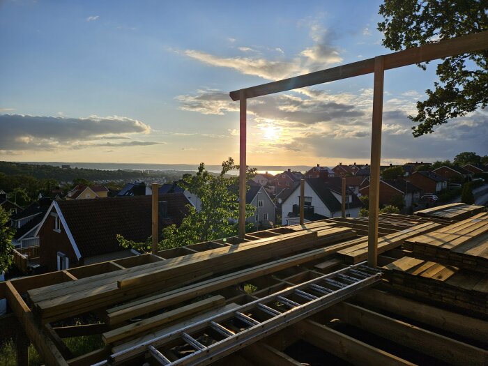 Konstruktion av pergola med tjocka träreglar och stolpar mot solnedgång i bostadsområde.