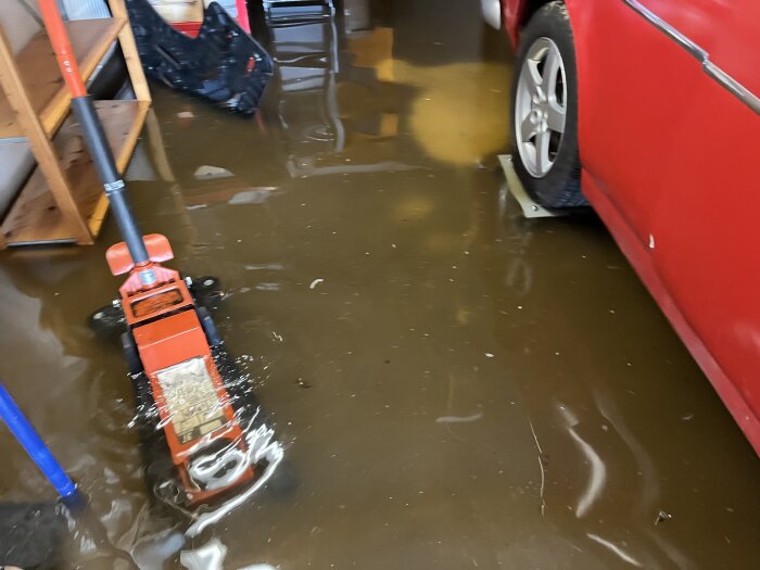 Översvämmat garage med vatten runt en bil och en pallbock.