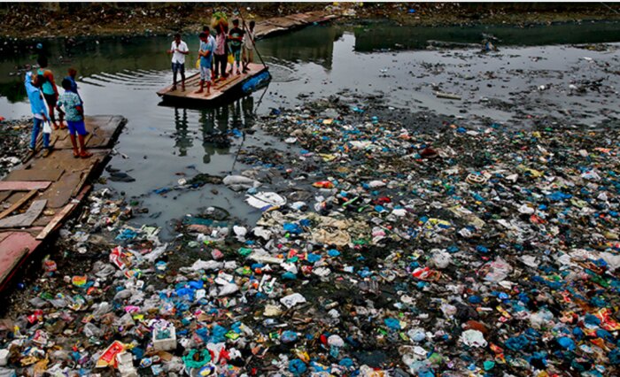 Människor på en flotte omgiven av ett förorenat vattenområde täckt med plast och annat skräp.