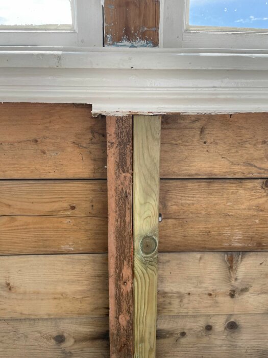 Närbild på en verandastomme där en gammal, rötangripen regel delvis har ersatts med nytt virke under ett fönster.