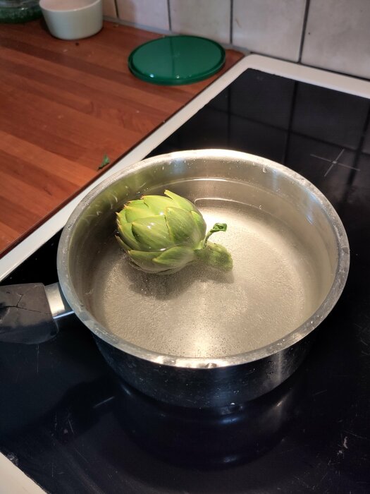 Artichoke i en kastrull med vatten på en spishäll, redo för tillagning.