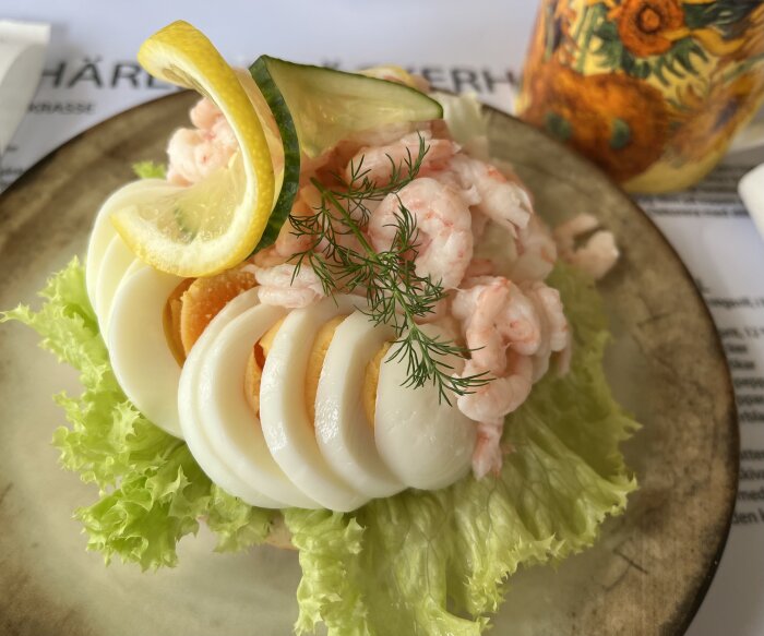 Räkmacka med ägg, citron och dill på salladsblad serverad på en tallrik.