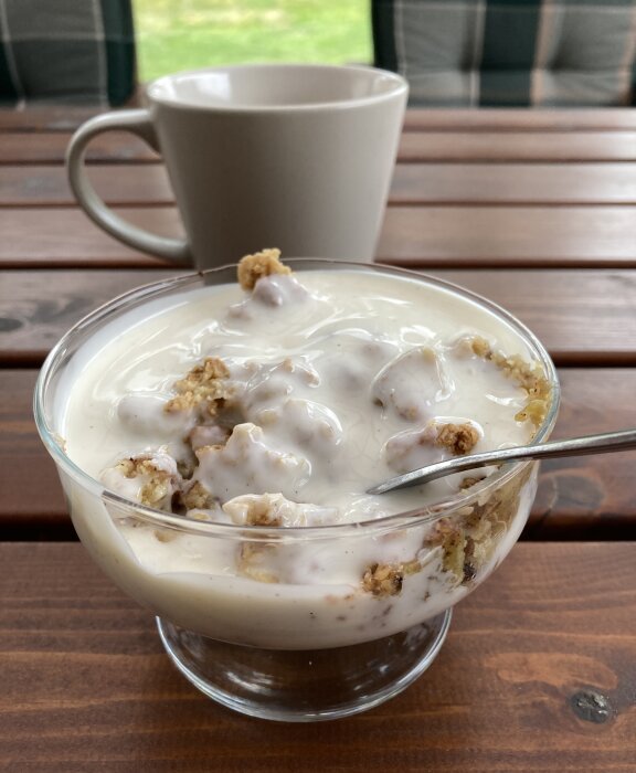 Rabarberpaj med vaniljsås i ett genomskinligt glas, sked och kaffekopp i bakgrunden.