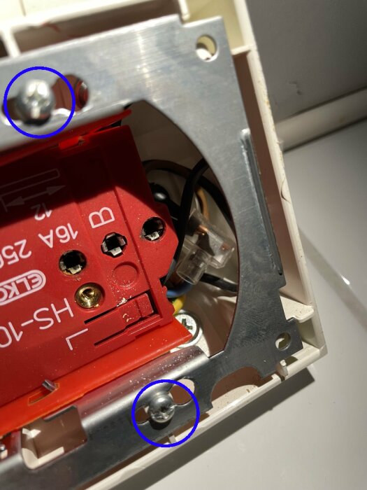 Närbild på en elektrisk anslutning med två markerade skruvar som ska lösgöras för att kunna vrida och dra ut kontakten.