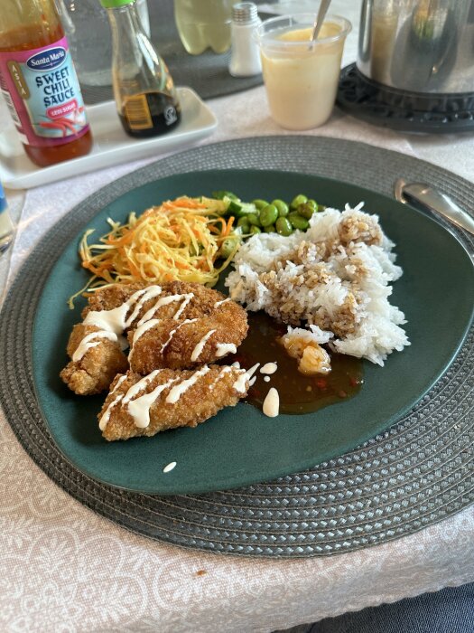 Tallrik med friterad kyckling, ris, grönsaker och sås på ett bord med duk.