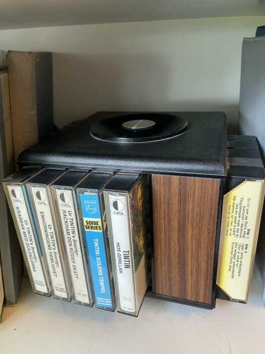 Gammal kassettsnurra med ett urval av Tintin ljudbokskassetter på en hylla.