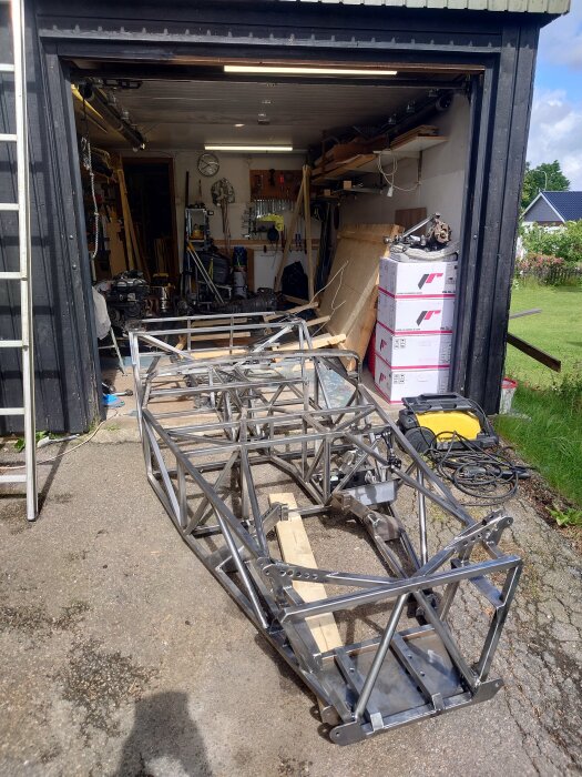 Metallramkonstruktion för arbetsbänk ligger utanför ett garage fyllt med verktyg.