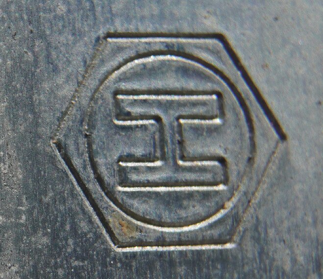 Närgräns tagen bild av en logotyp inpräntad på metall med bokstäverna "SF" inuti en hexagon.