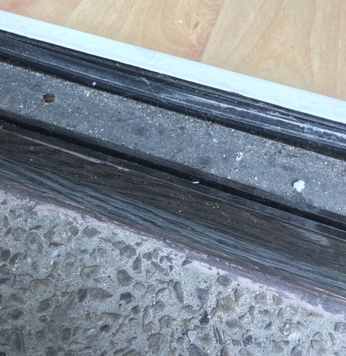 Nötningsmärken och smuts på en altandörrs tröskel mellan inomhus trägolv och utomhus betong.