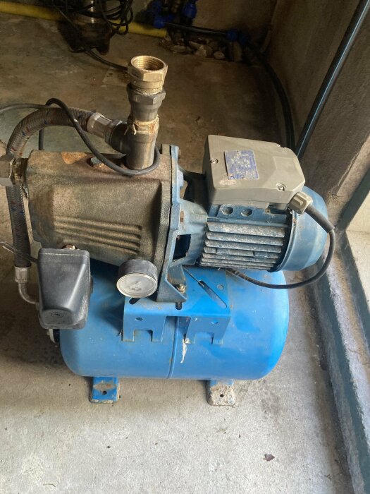 Begagnad blå pumpautomat med motor och trycktank för brunnsvatten, placerad på ett betonggolv.