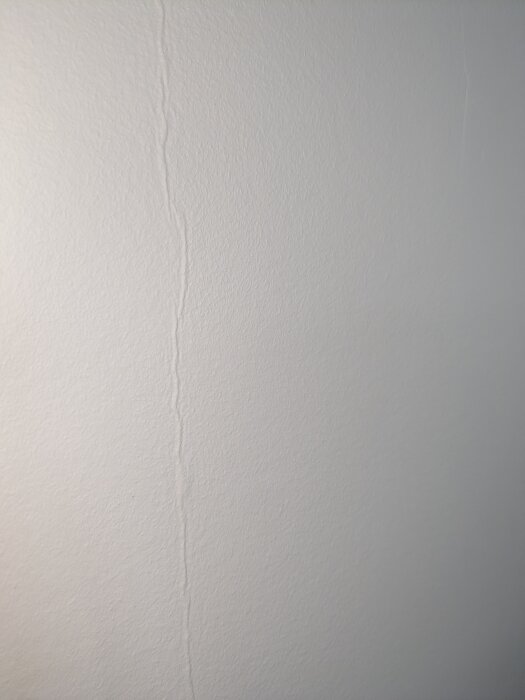 Närbild på en vitmålad vägg där en lodrät skarv i renoveringstapeten syns, vilket skapar en veckad effekt.