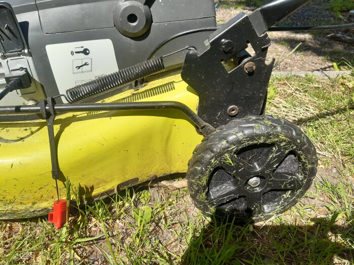 En gul gräsklippare med ett nytt, svart 3D-utskrivet bakhjul, omgiven av gräs.