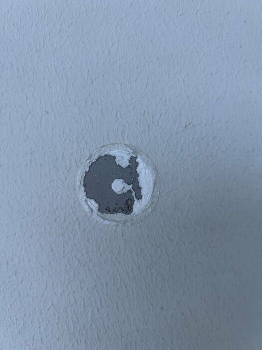 Närbild av en liten rund skada på en vägg där färgen har lossnat efter att en självhäftande skruv har tagits bort.