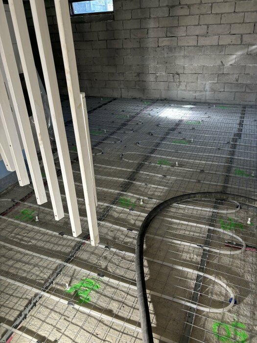 Golvkonstruktion med golvvärmeinstallation i källare, isobeton som bas med rör för golvvärme och gröna markeringar på marken.