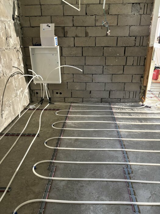 Installation av golvvärme på betonggolv i en källare, med ett elskåp monterat på en rå vägg av betongblock i bakgrunden.