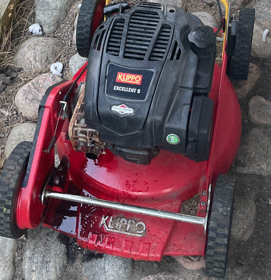 Röd gräsklippare av märket Klippo med en oljefläck på marken under maskinen, indikerande ett problem med oljeläckage.