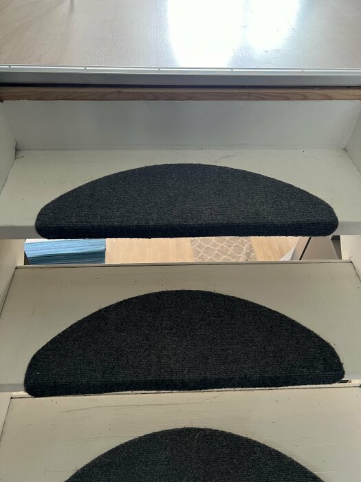 Närbild på slitna trappsteg med svarta trappstegsmattor, ljusare laminatgolv syns på översta trappsteget.