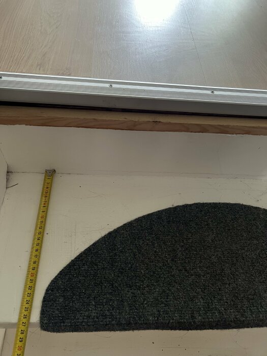 En halv måttband ligger längs ett trappsteg och mäter cirka 21 cm brett. Trappsteget är delvis täckt med en halvcirkelformad matta.