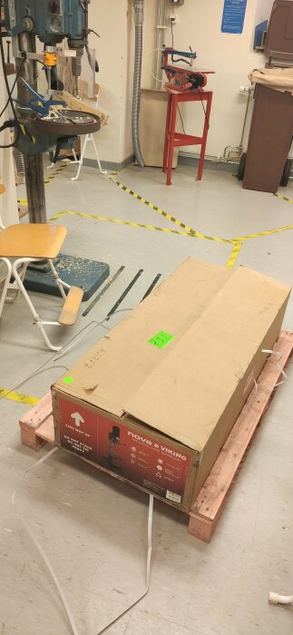 Stort paket med en Nova Viking digital borrmaskin på en pall inuti ett klassrum med olika verktygsmaskiner.