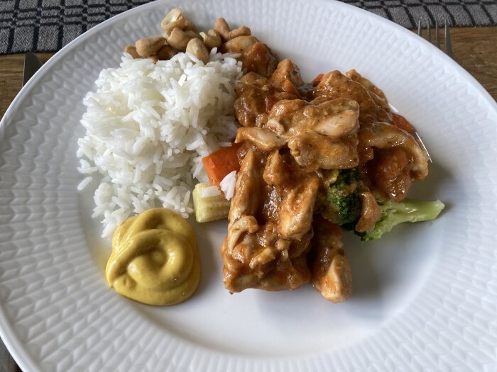 Tallrik med Chicken Tiki masala, ris, cashewnötter, grönsaker och en klick sås.