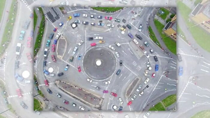 Flygfoto av en stor trafikplats med flera små rondeller runt en central större rondell, många bilar i olika färger och storlekar kör i olika riktningar.