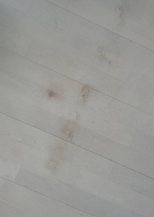Slitet vitlackerat golv med fläckar och repor i träet.