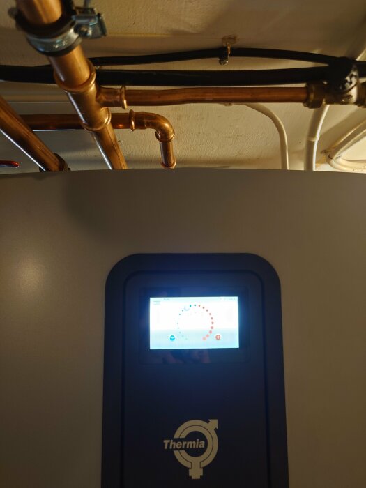 Thermia Eco värmepump med kopparrör ovanför och en skärm som visar inställningar, fotograferad inomhus med lågt tak.