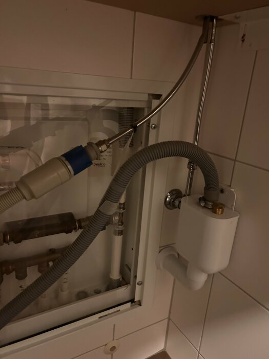 Avstängningsventil för tvättmaskin, med kopplade rör och slangar, samt en vit box på väggen för vattentillförsel.