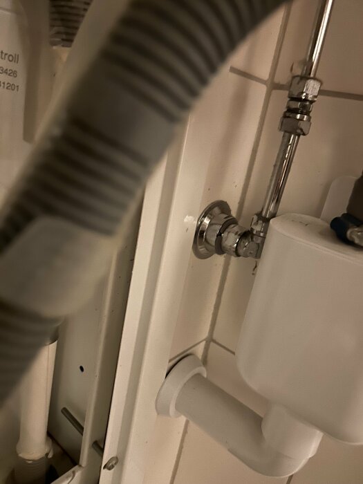 Ventilrör och avloppsrör vid tvättmaskin med avstängningsventil och vit box synliga i ett badrum.