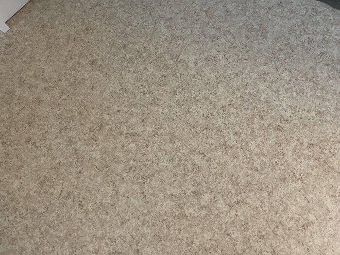 Beige- och brunmönstrad plastmatta på golvet, med en fråga om den kan innehålla asbest eller vara en linoleummatta.