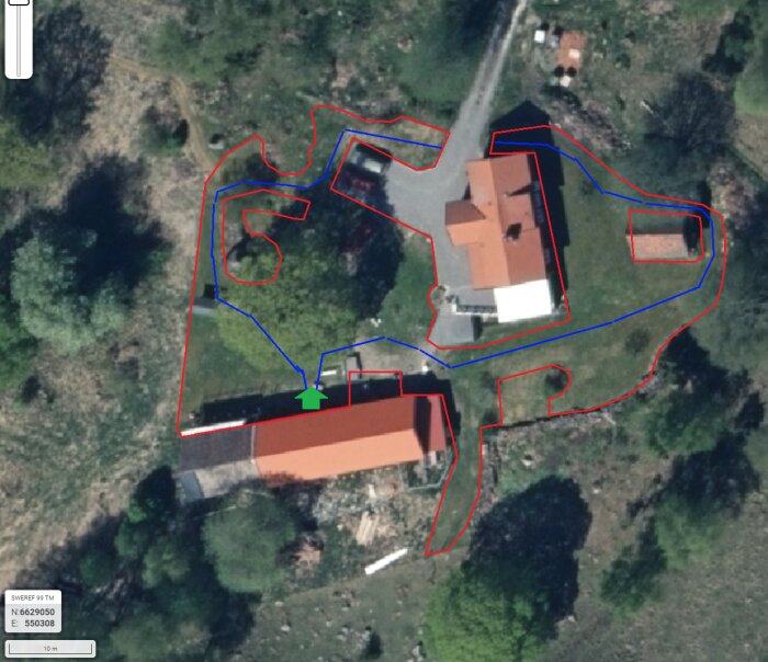 Satellitkarta över en tomt med två byggnader; röda linjer visar begränsningskabel och blå linjer guidekablar för robotgräsklipparen.