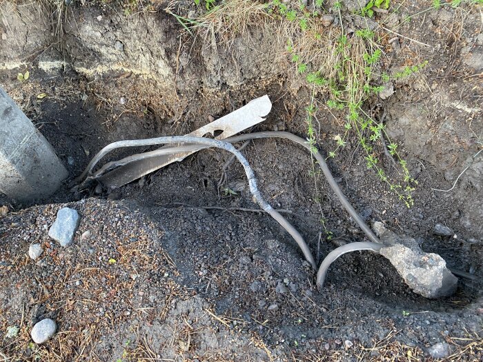 Kabelskarvar och extrakabel vid utgrävning nära stolpe, med vegetation och sten ovanför jorden.