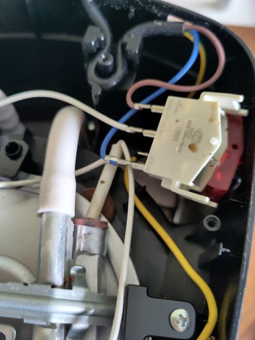 Inre delen av en apparat som visar elektroniska komponenter och kablar samt ett litet brännmärke på en vit kabel.