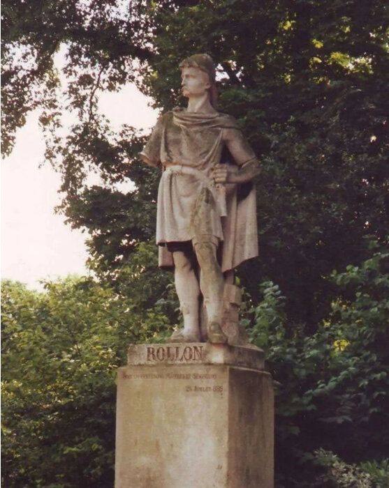 Staty av Rollon på en stenpedestal omgiven av träd i en park.