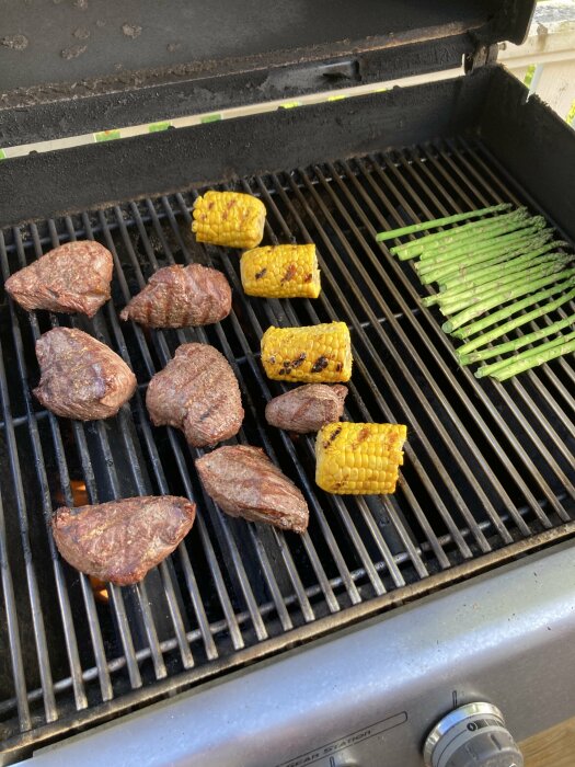 Grill med rostasbitar, majsbitar och sparris som grillas på gallret.