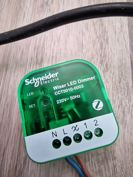 Schneider Electric Wiser LED Dimmer modell CCT5010-0003 med anslutningsportar och kablar, placerad på ett träbord.